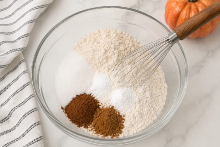 Flour, sugar, cinnamon, baking soda, baking powder, salt, and pumpkin pie spice in a mixing bowl for moist pumpkin bread.