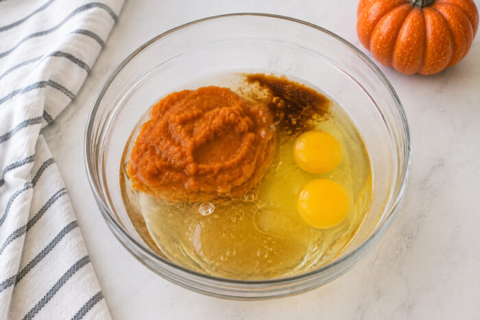 Pumpkin puree, vegetable oil, vanilla extract, eggs, and water in a mixing bowl before mixing for moist pumpkin bread.
