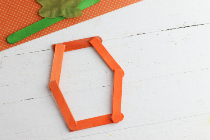 Orange popsicle sticks assembled into a pumpkin-shaped frame for an easy fall craft