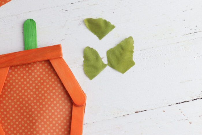 Faux green leaf cut into smaller pieces to decorate the top of a popsicle stick pumpkin