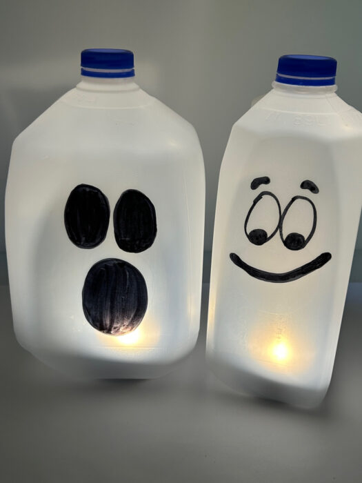 Two glowing milk jug ghosts with different black ghost faces and flameless lights inside.