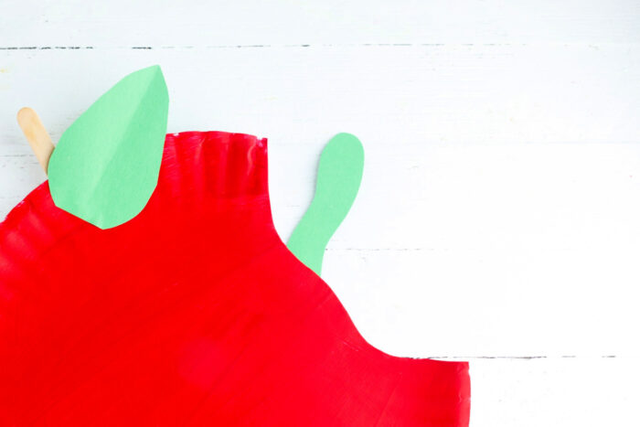 Green paper caterpillar peeking out of the bite in a red apple paper plate craft