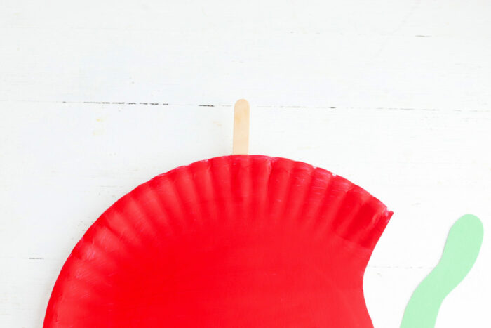 Craft stick attached to the red paper plate to create the stem for the apple paper plate craft