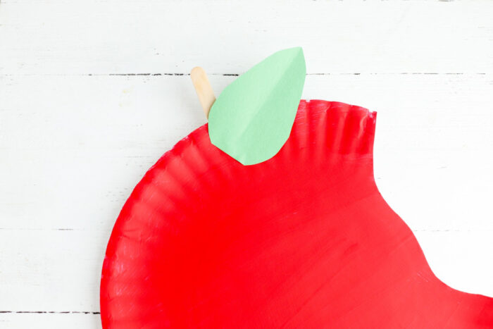 Craft stick stem and green paper leaf glued onto the red apple paper plate craft